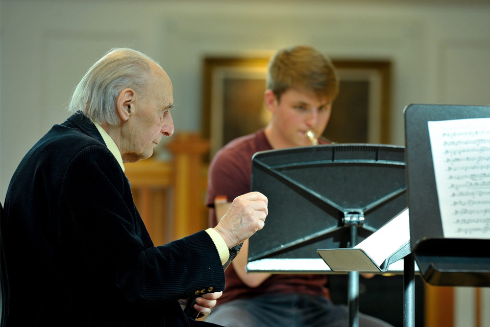 Image of Joseph Horovitz conducting with a brass student visible in the background