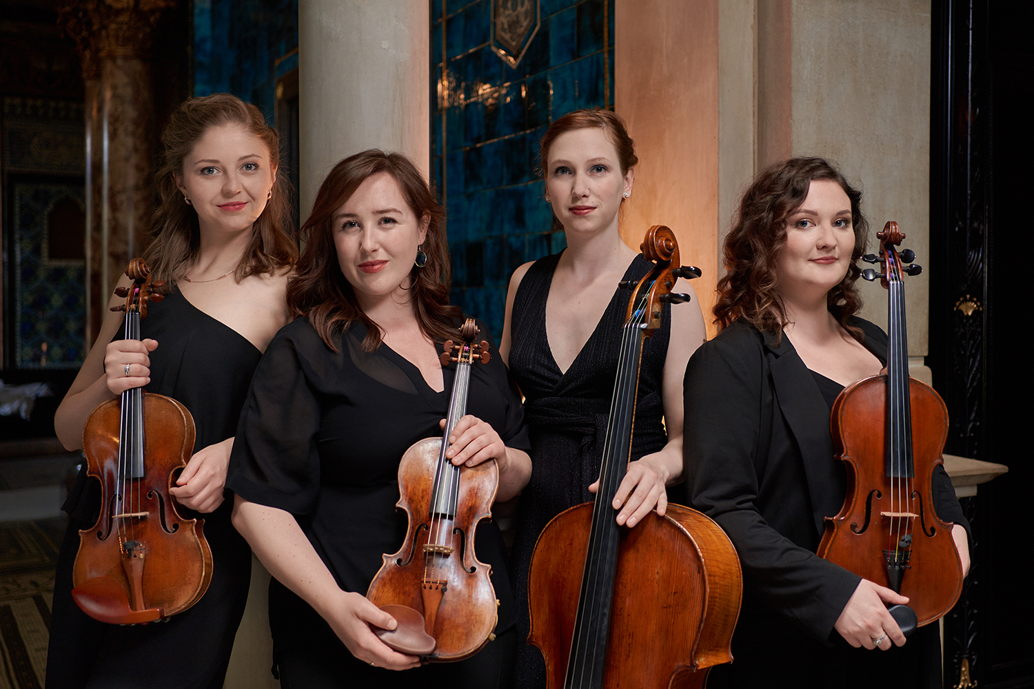 Four women musicians who comprise Alkyona Quartet holding their string instruments and wearing black