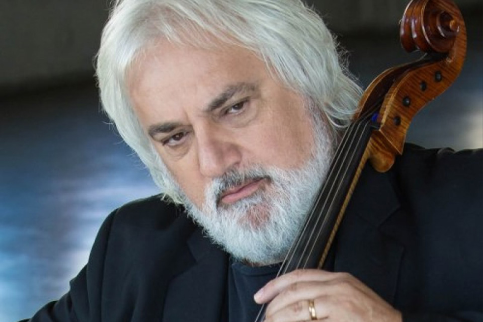 Andrew Shulman wears a black blazer and plays his cello with a serious expression