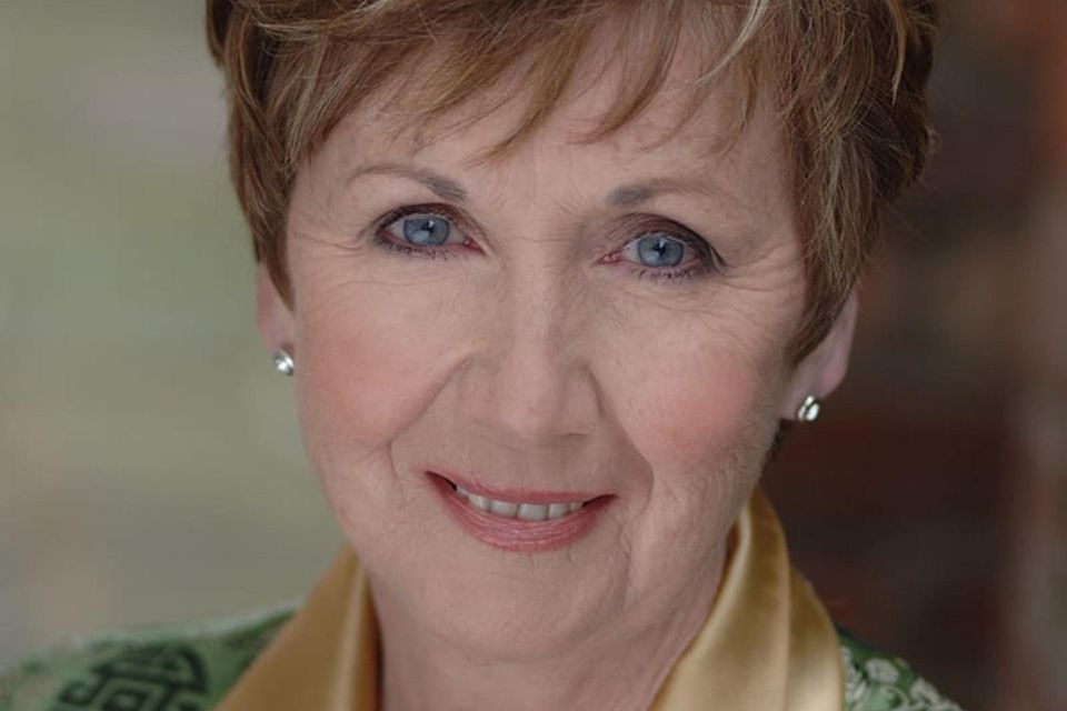 Ann Murray wears pearl earrings and a yellow scarf and smiles