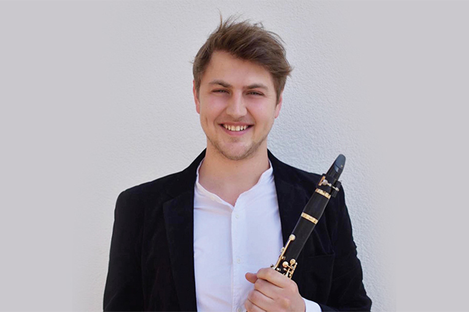 Benjamin Mellefont wears a white shirt and black blazer and holds his clarinet, smiling