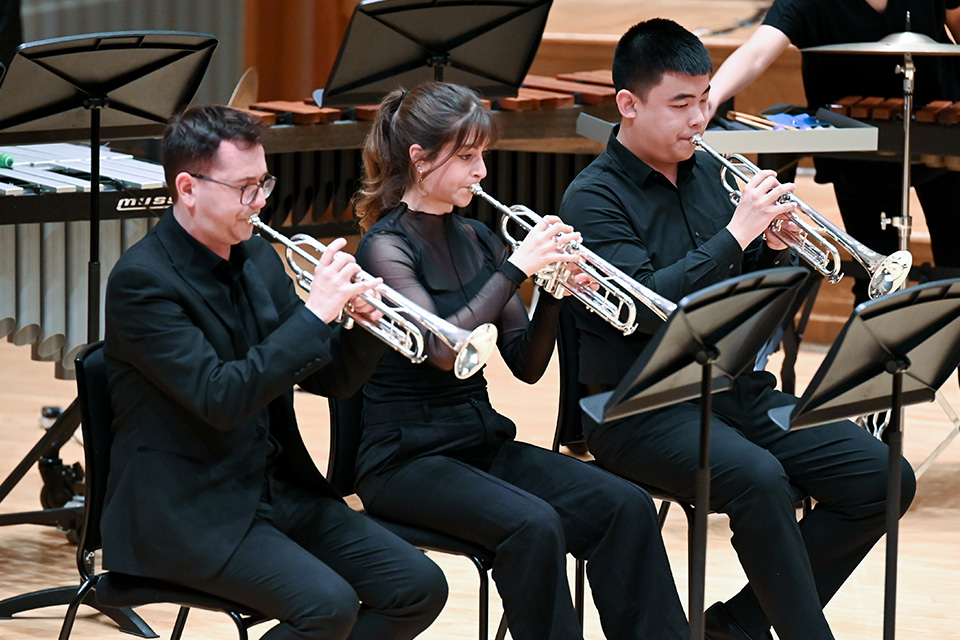 Three trumpeters perform on stage wearing black as part of a brass ensemble