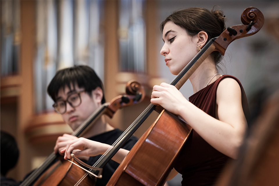 Two cellists perform on stage as part of an orchestra