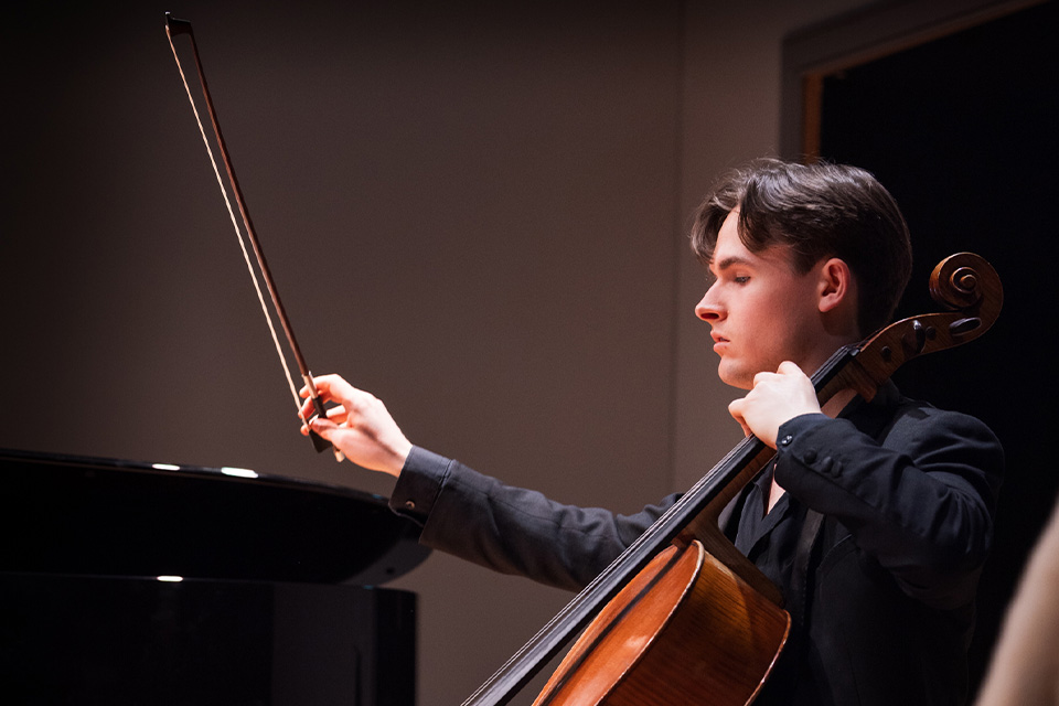 A young man playing the cello raises his bow in the air