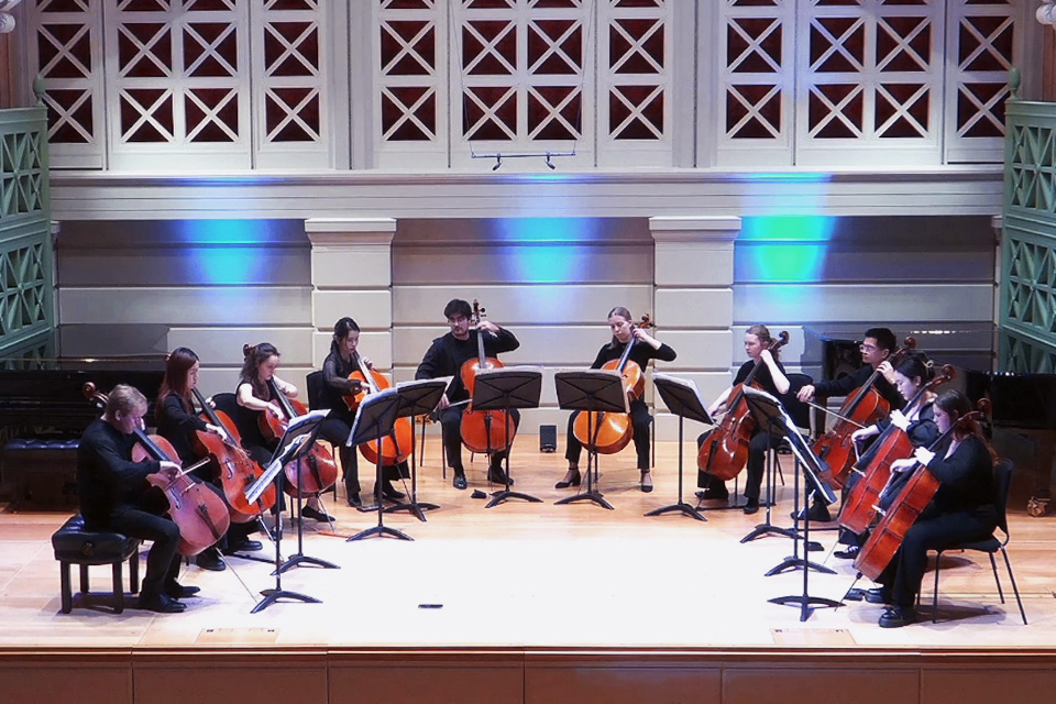 A cello ensemble of ten cellos perform in a semi-circle on stage