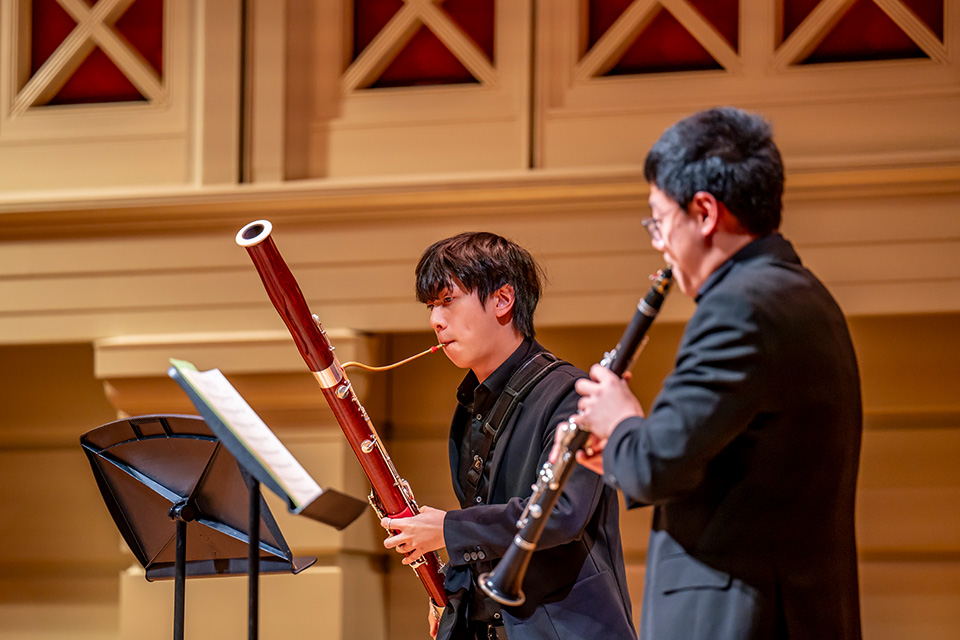 A bassoonist and clarinettist perform on a brightly lit stage
