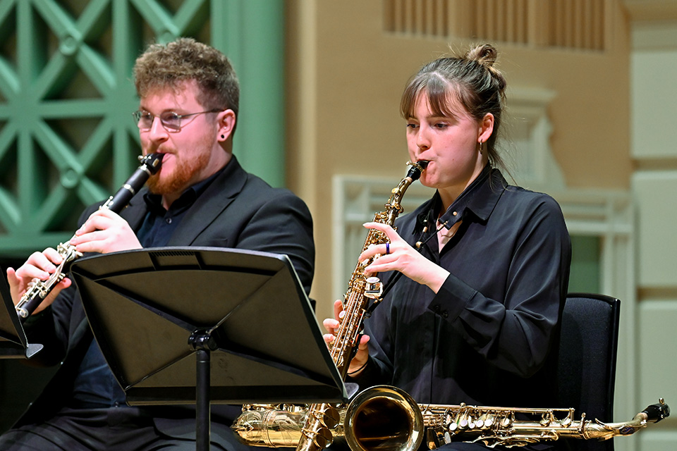 A clarinetist and saxophonist wear black and perform on stage in the RCM Performance Hall