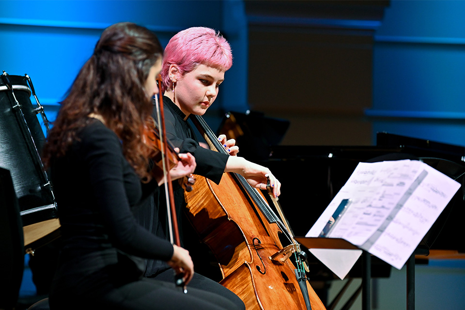 A violinist and cellist perform on a brightly lit stage