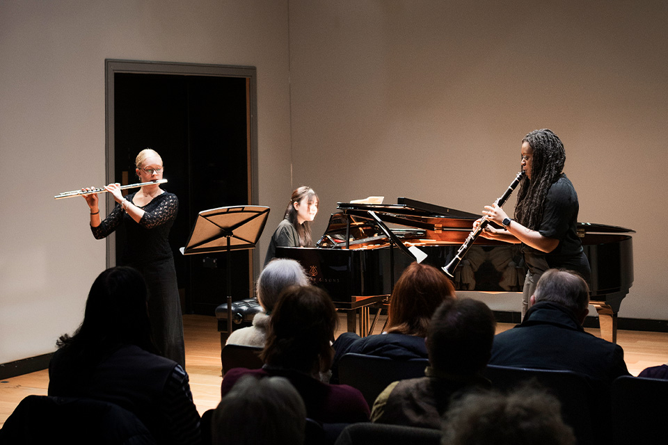 A flautist, clarinetist and pianist wear black and perform to an audience in the RCM Performance Studio