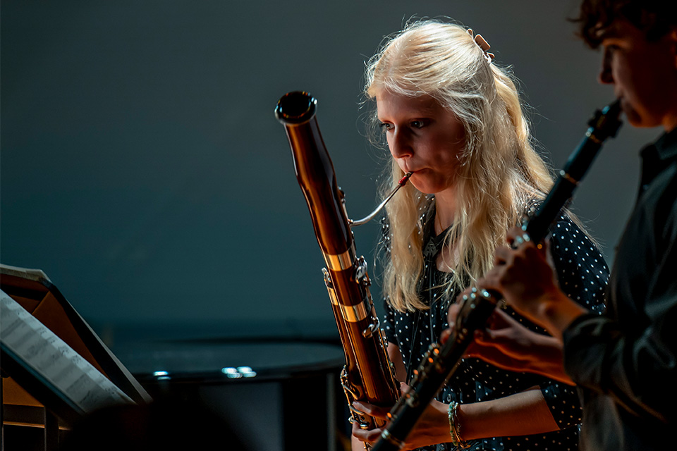 A young woman plays the bassoon in a dark room