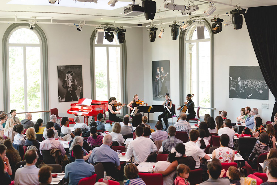 A string quartet performs in the brightly lit Elgar Room of the Royal Albert Hall, while an audience listens attentively