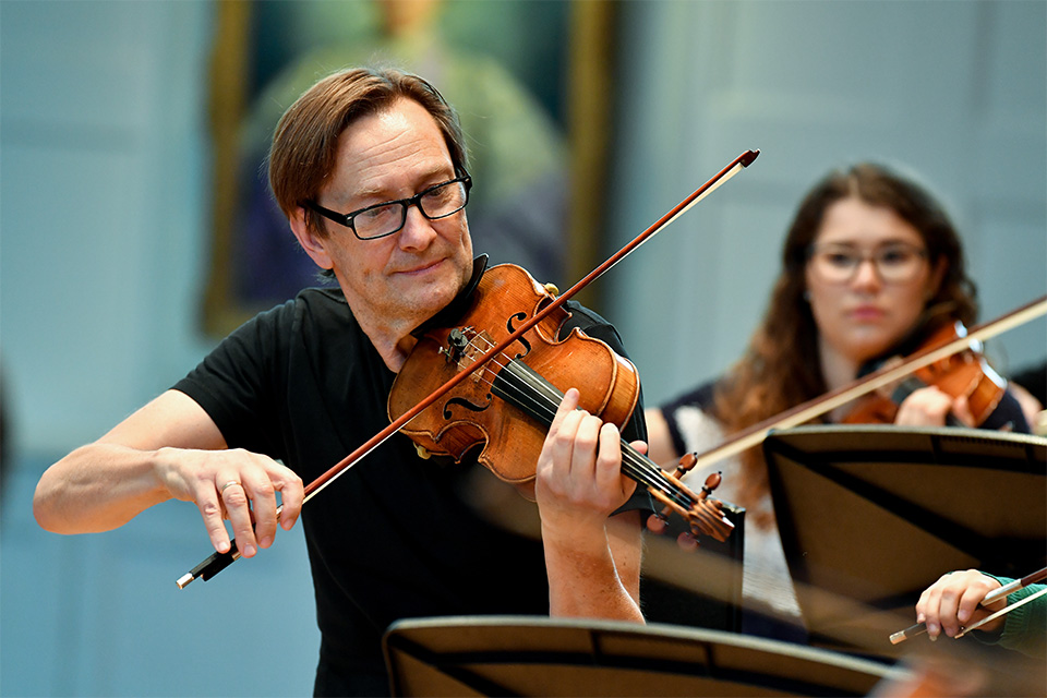 A man wearing a black t-shirt performing on the violin