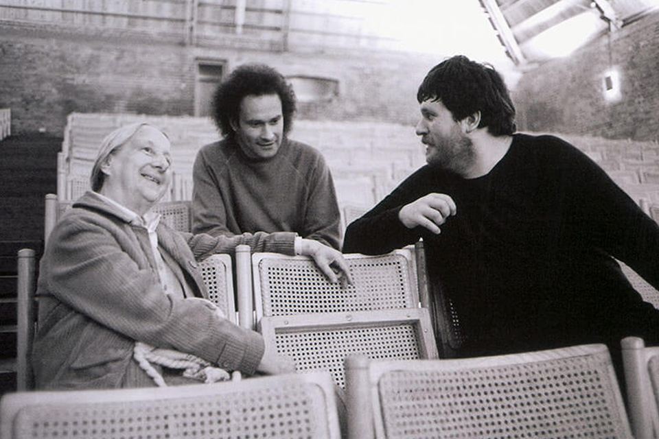 Three people sit on chairs in an auditorium chatting and smiling