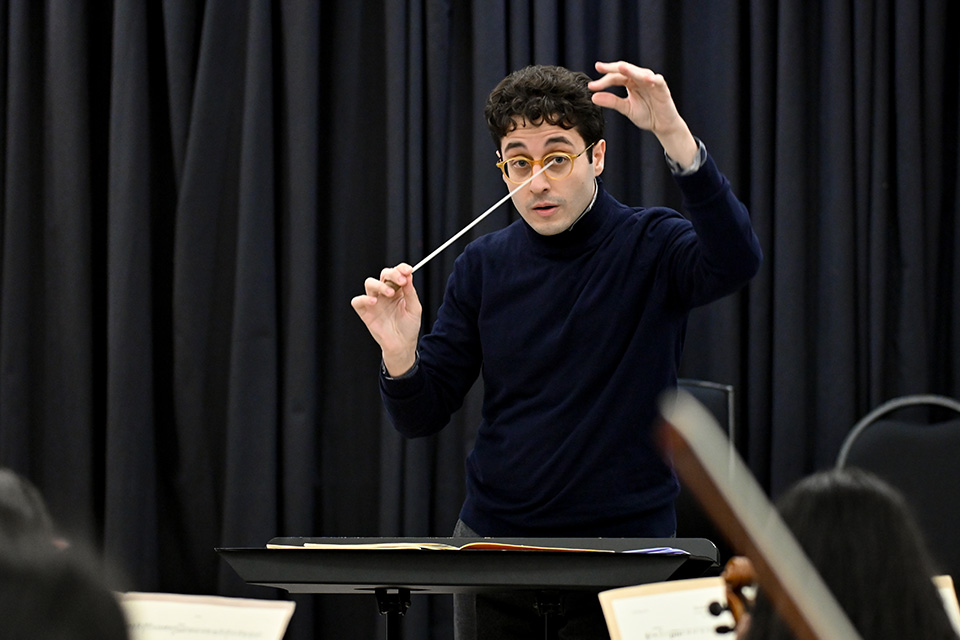 A young man conducts passionately in front of a blue curtain