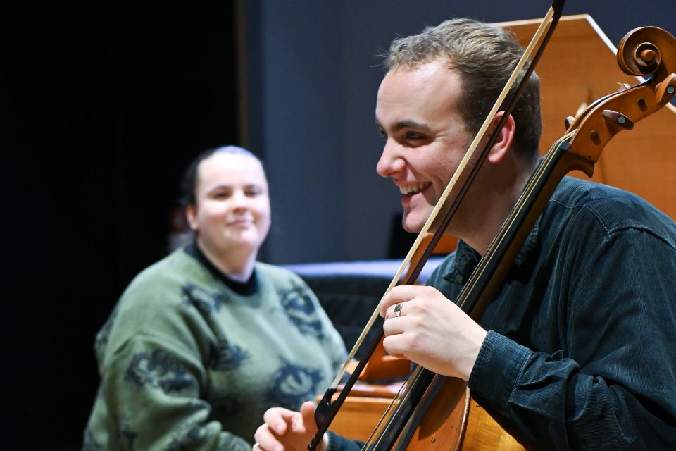 A young man laughs as he holds a baroque cello and bow