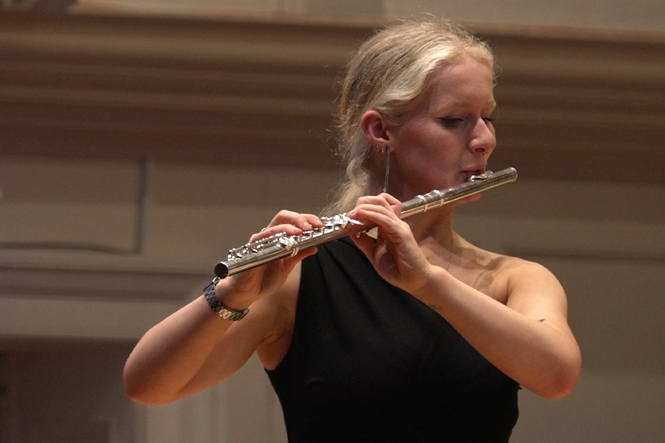 A woman wearing a black top performs the flute