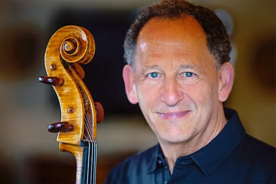 Denis Brott wears a black shirt and holds his cello, smiling softly