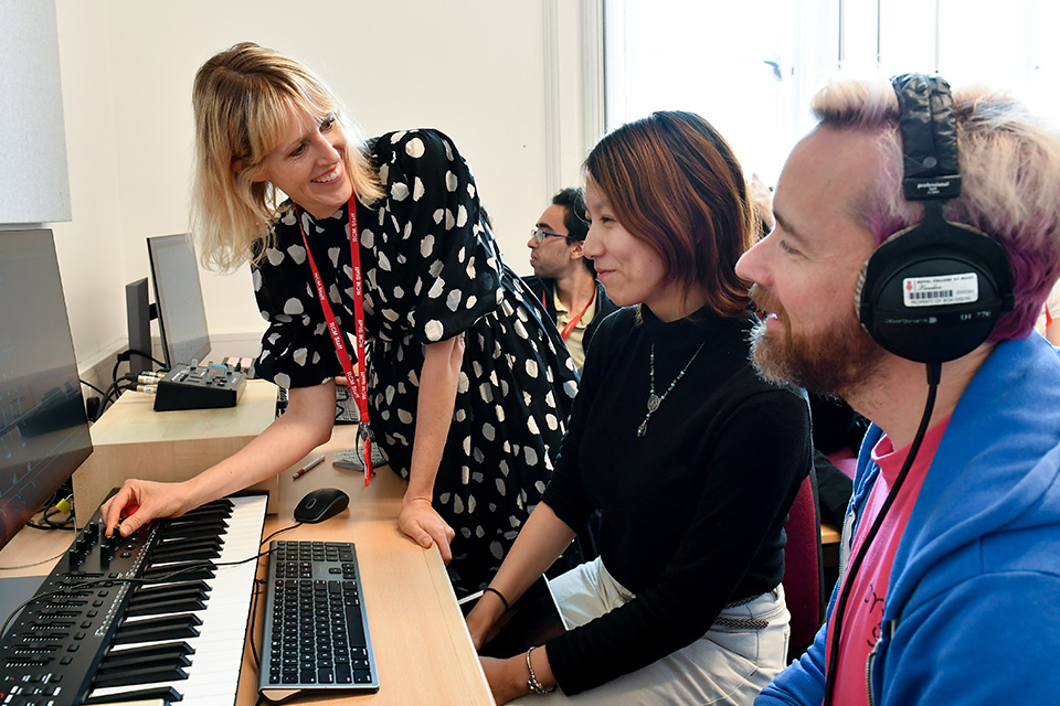 A woman shows students something on a computer with a piano keyboard in front of it