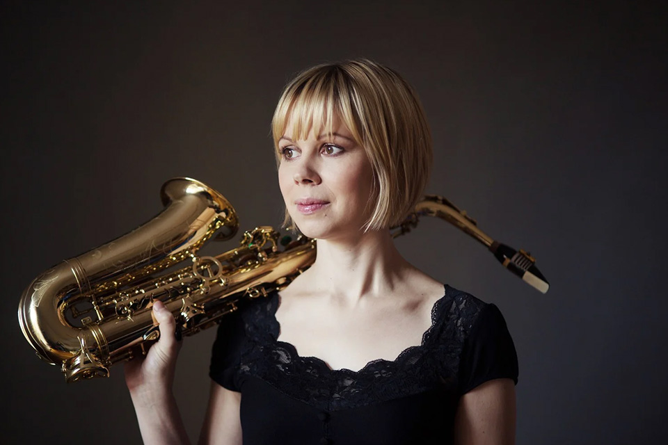 Erzsébet Seleljo, wearing a black top, holds her saxophone up to her shoulder