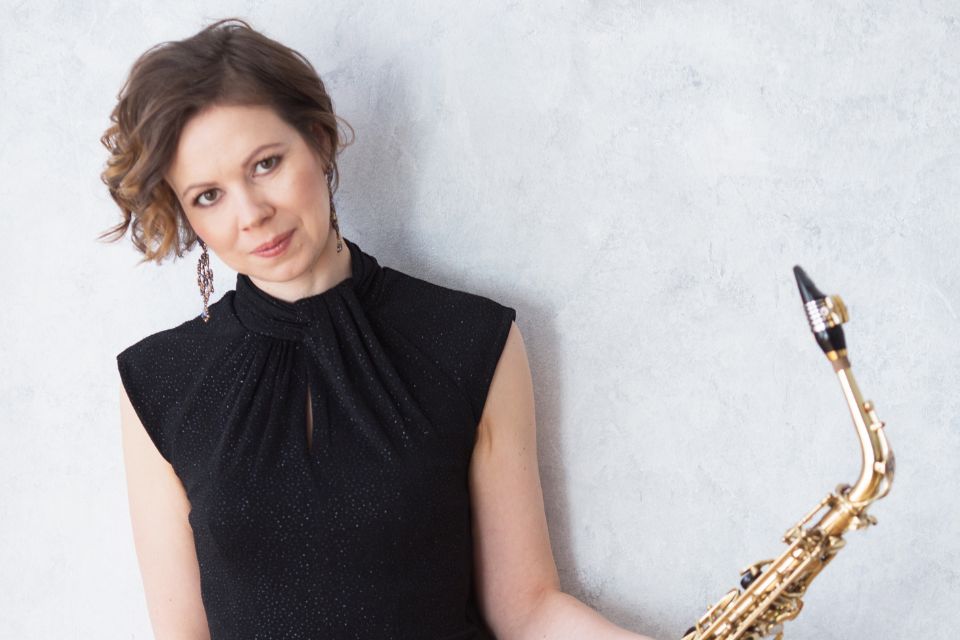 Erzsébet Seleljo, wearing a black top, holds her saxophone up to her shoulder