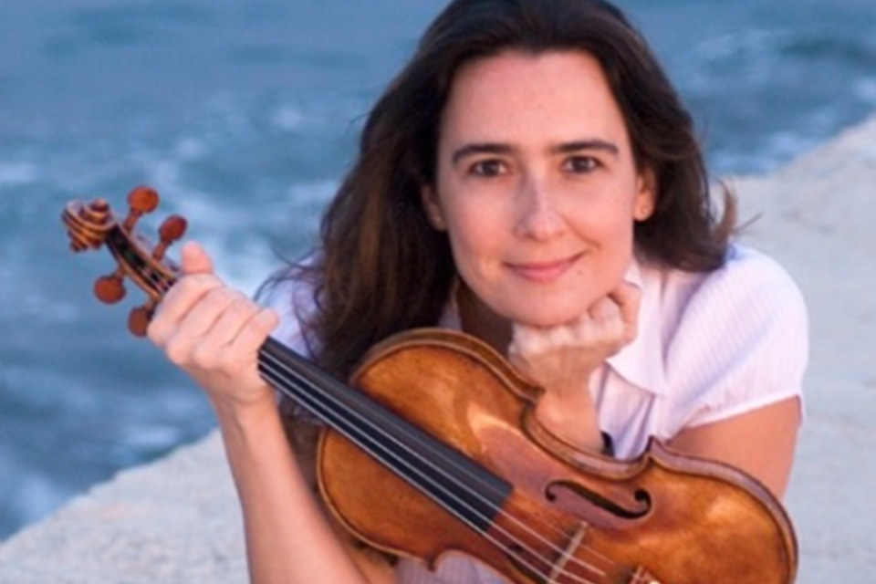 Eszter Haffner holds her violin under her chin and smiles, a blue lake behind her