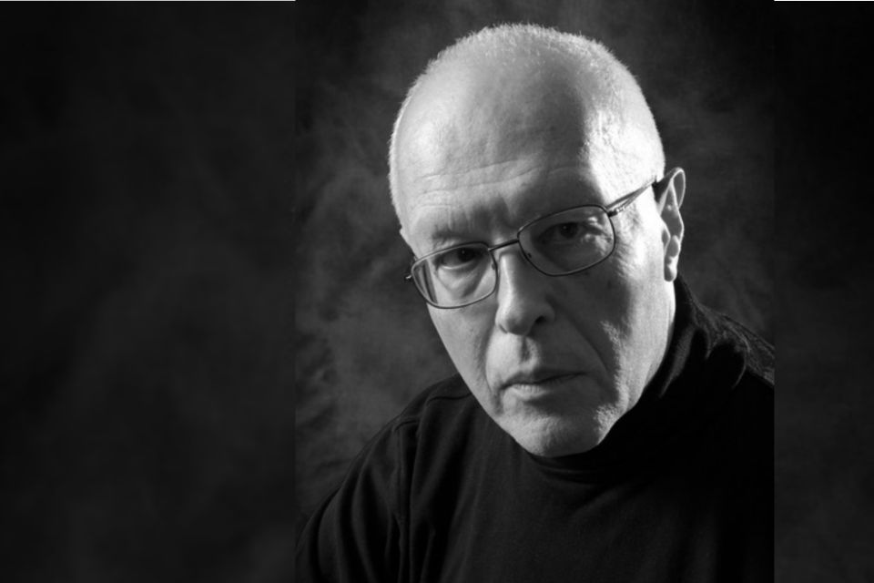 A black and white photo of Michael Finnissy wearing a black turtleneck and glasses