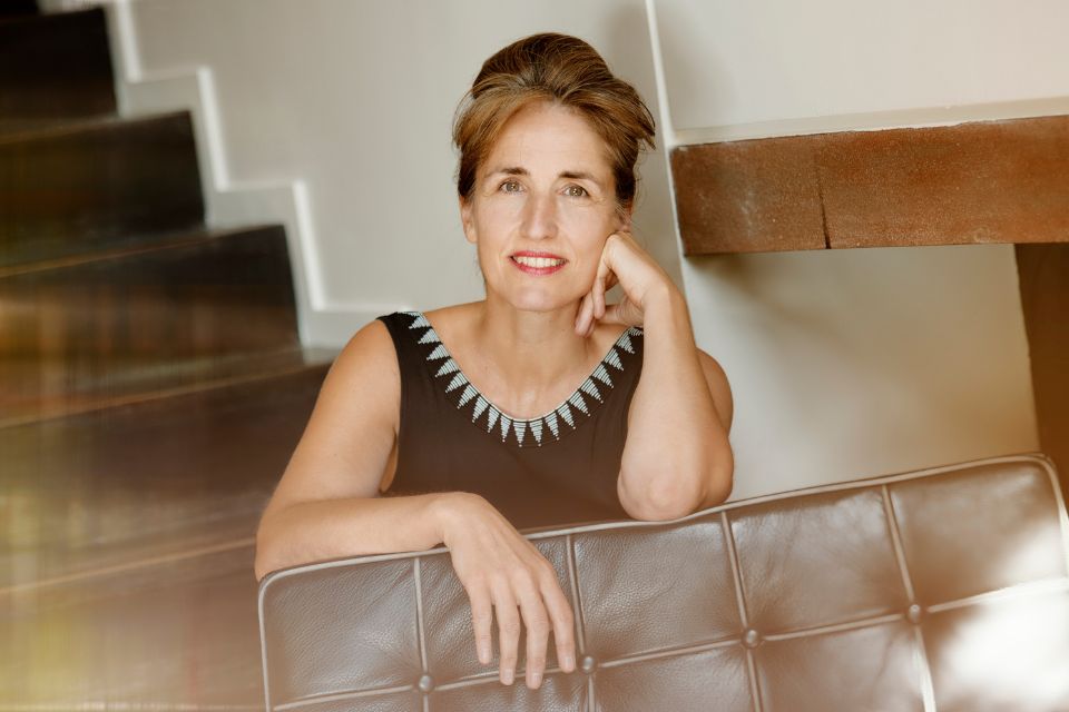 Florence Millet leans on the back of a sofa resting her chin on her hand and smiling