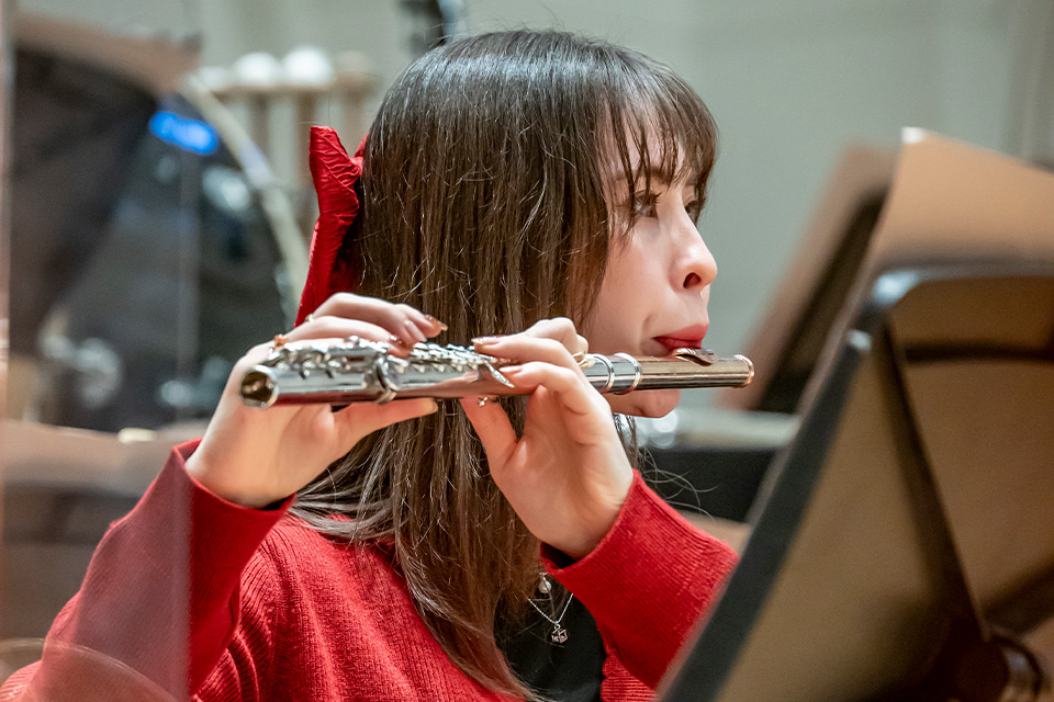 A young woman wearing red plays the flute
