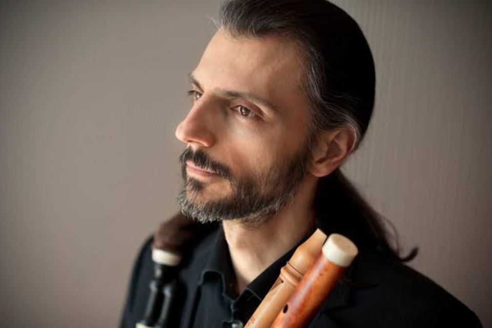 François Lazarevitch holds two historical fltues and looks up, smiling