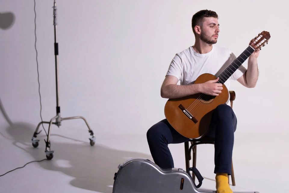 Arie Dakesian wears a white shirt and sits playing his guitar