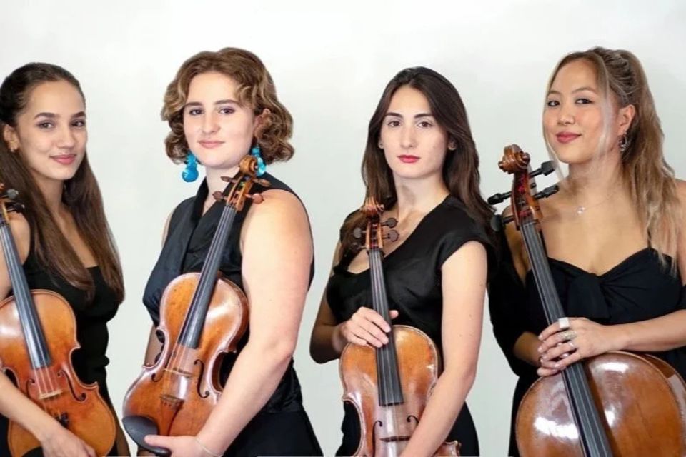 The Fiora String Quartet wear black and stand holding their instruments against a white background