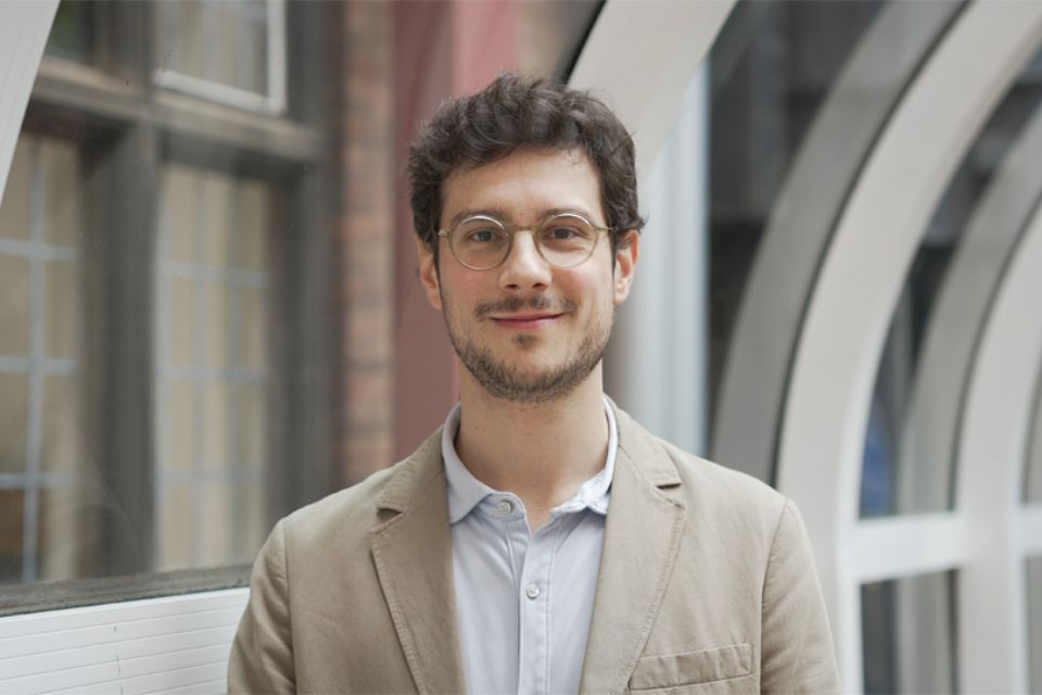Gerardo Gozzi, wearing a beige jacket, smiles to camera