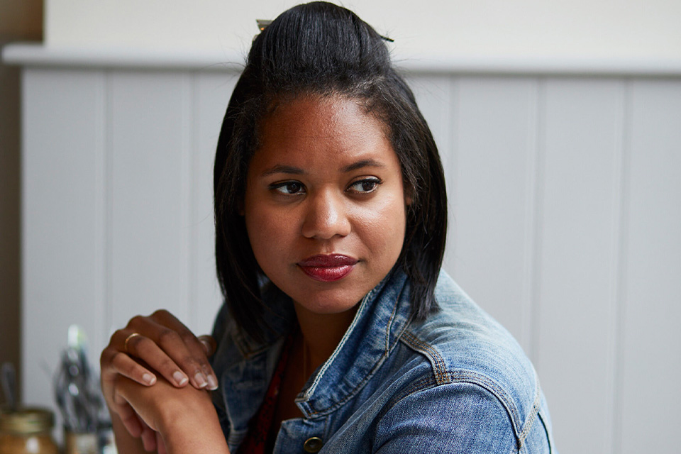 Hannah Kendall sits at a table with her hands clasped, looking over her shoulder