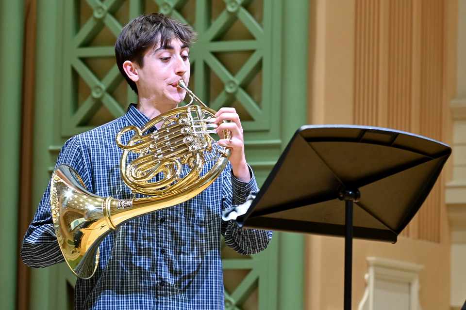 A young man wearing a blue shirt plays the horn on stage