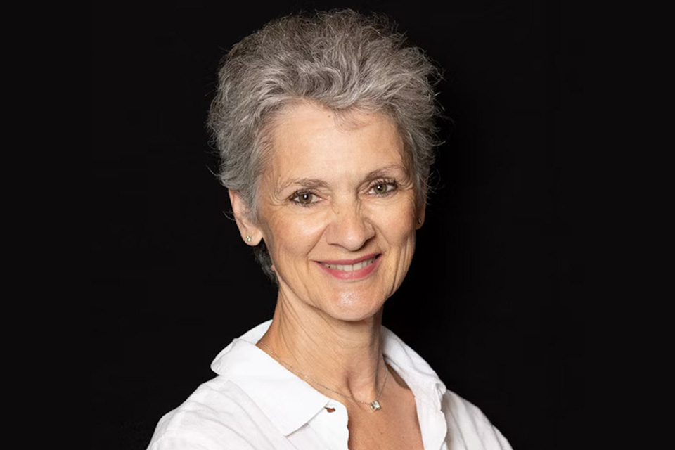 Isabelle Perrin wears a white shirt and smiles against a dark background