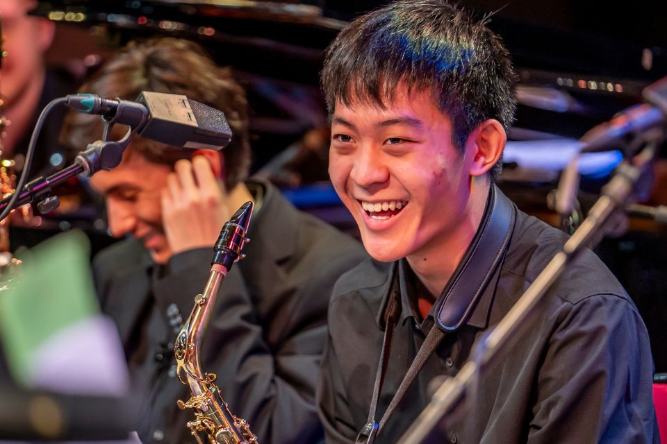 A young man holding a saxophone laughs