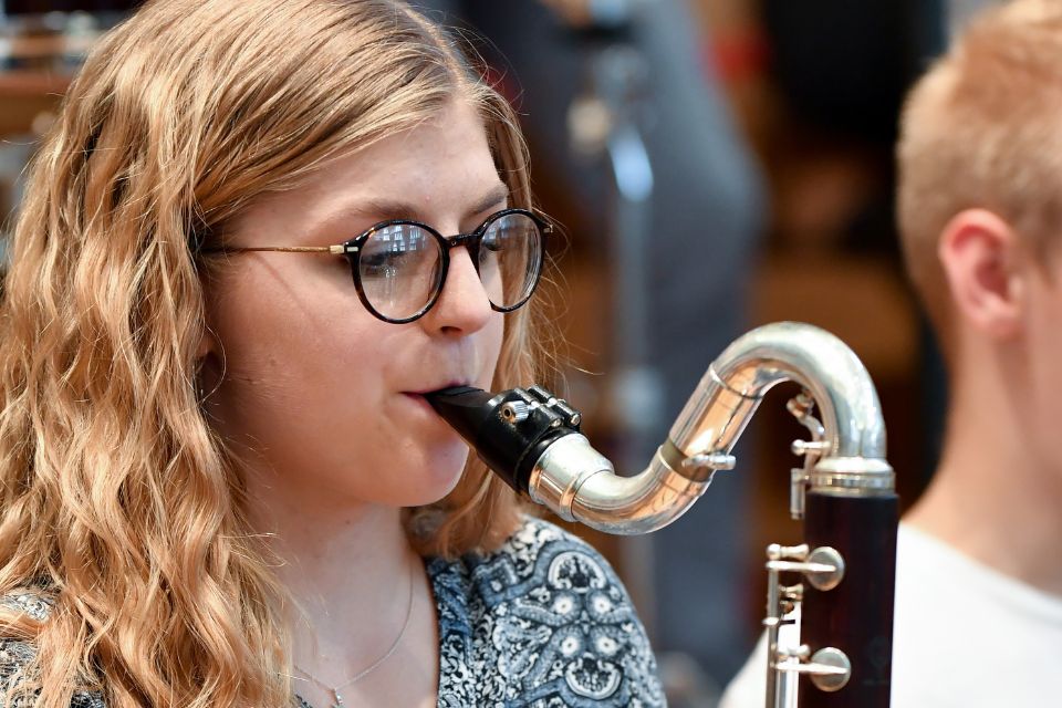 A young girl with blonde hair and glasses plays the clarinet