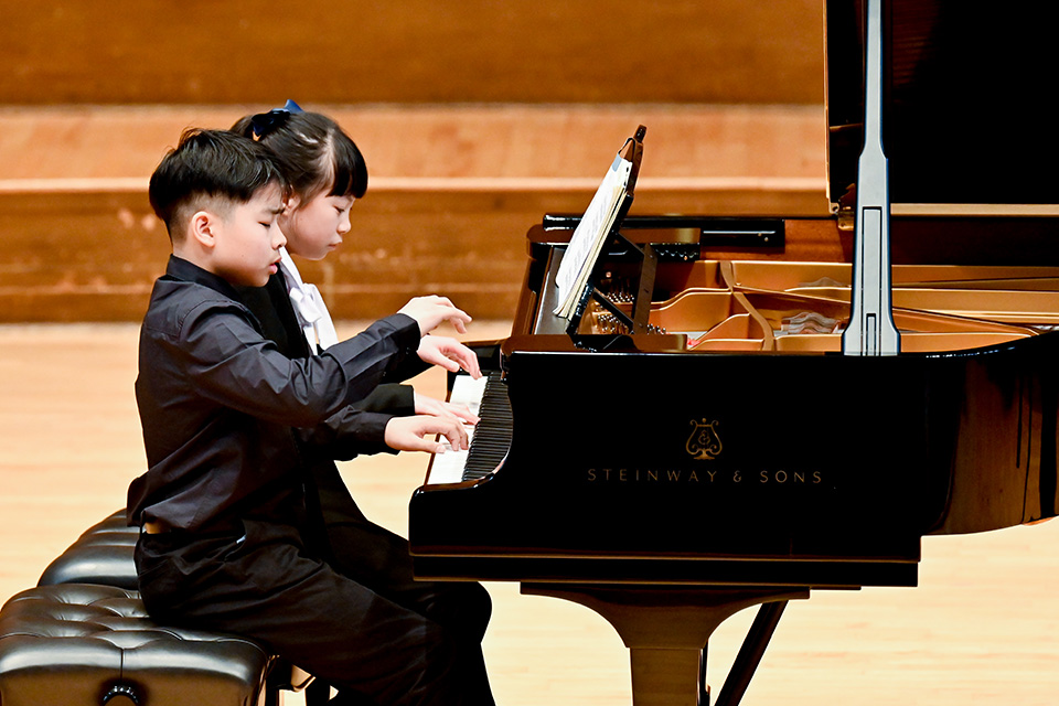 A young boy and girl play a piano duet on stage
