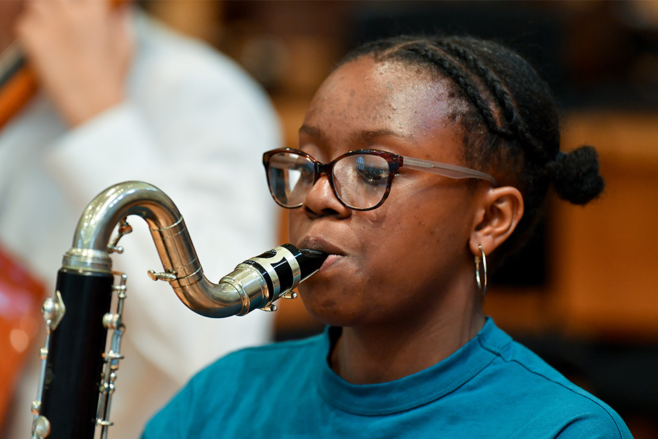 A young girl wearing glasses and a blue top plays the bass clarinet