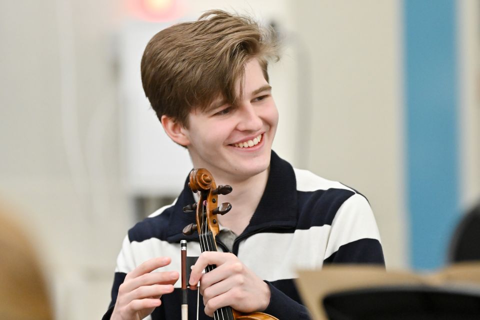 A boy smiles holding a violin