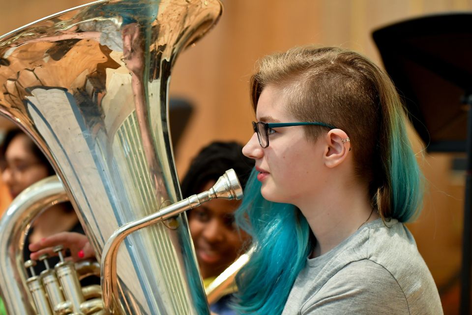 A girl with blue hair holds a tuba