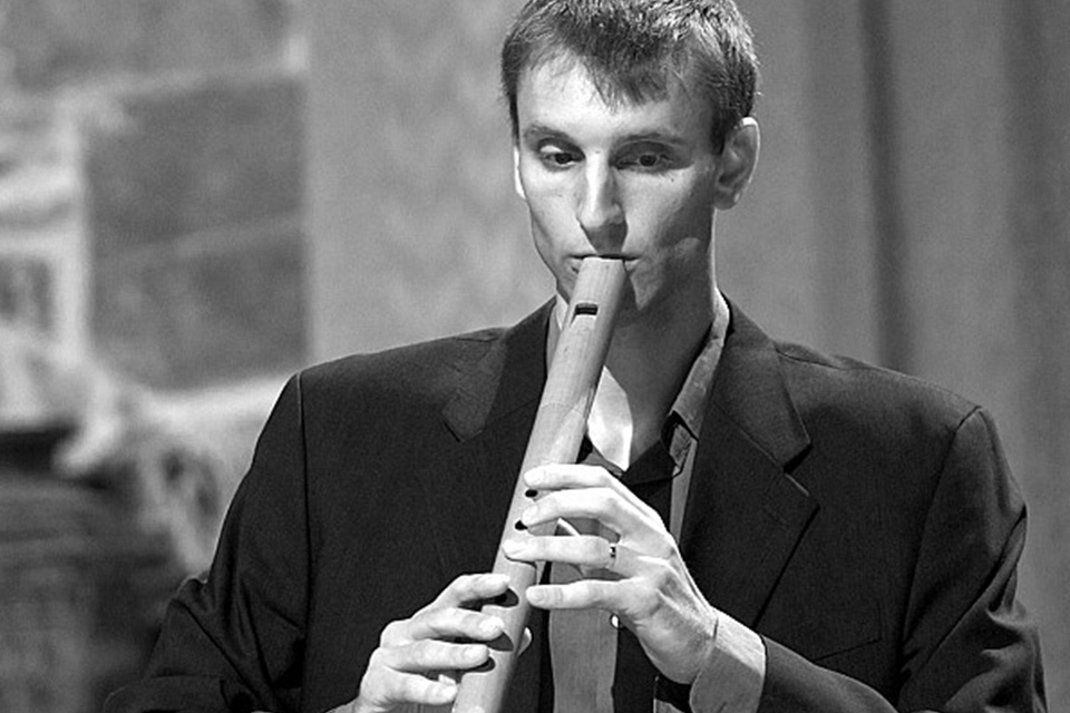 Jostein Gundersen wears a dark blazer and looks down as he plays his recorder