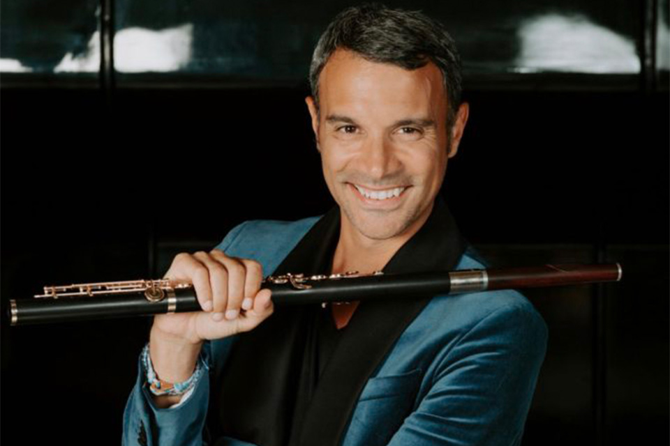 Julien Beaudiment wears a teal velvet blazer and holds his flute, smiling