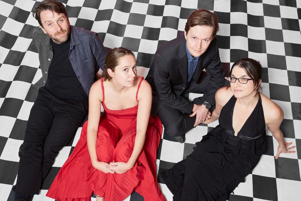 The Ligeti Quartet sit on a black and white checkered floor