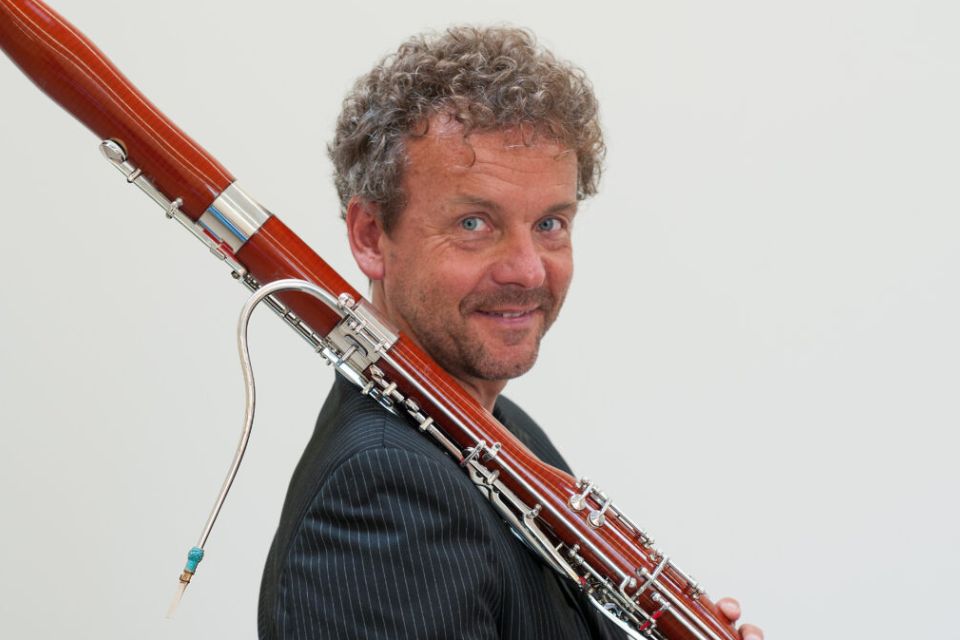 Marc Engelhardt holds his bassoon on his shoulder and looks over it against a light grey background