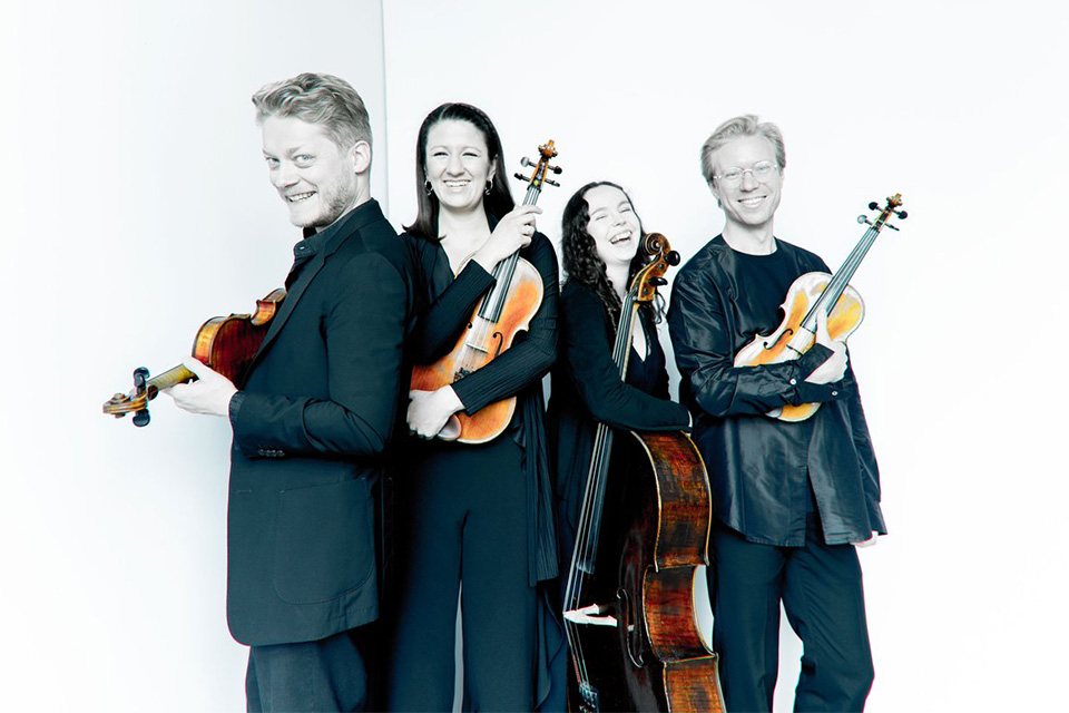 The Marmen Quartet stands in a bright room holidng their instruments and smiling