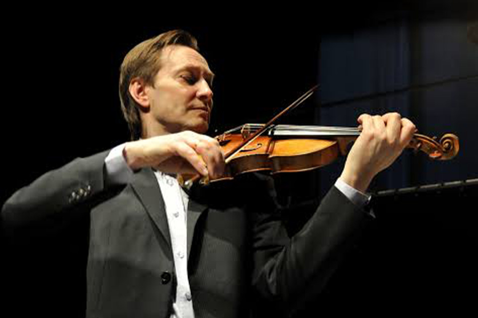 Mats Zetterqvist wears a black suit and plays his violin dramatically against a dark backdrop