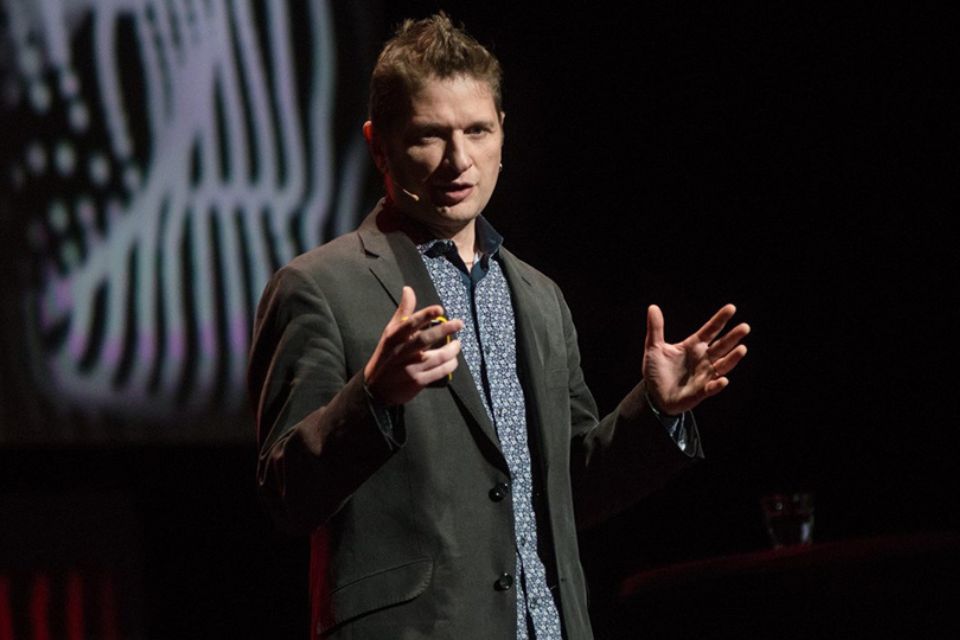 Milton Mermikides stands on stage and gestures as he speaks