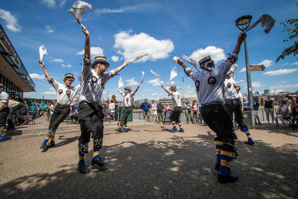 Four Morris dancers jump in a circle against a blue sky