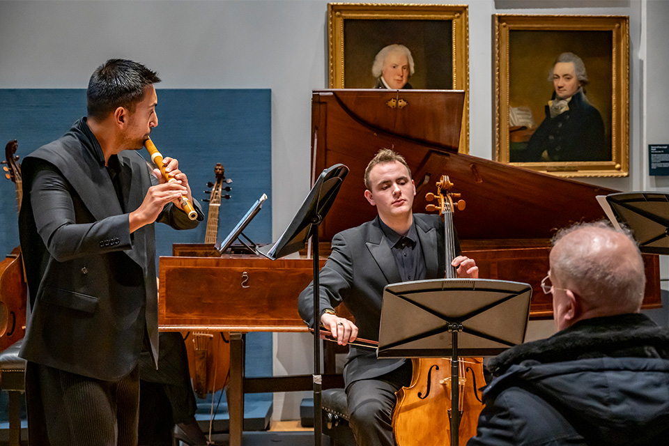 A three-piece baroque chamber group wear all black and perform in the RCM museum